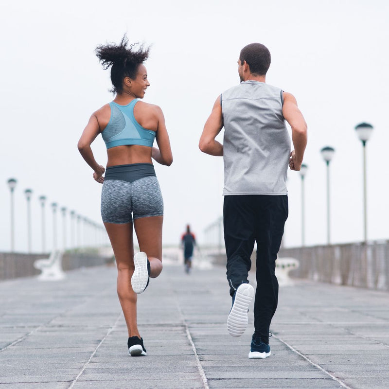 Man and woman jogging together on waterfront promenade in athletic sportswear