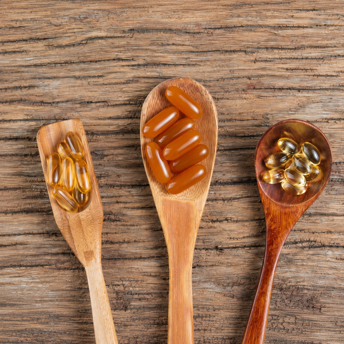 Three wooden spoons with assorted vitamin and supplement capsules on rustic background